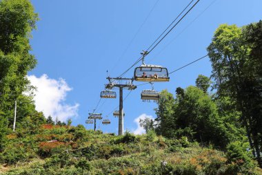 Krasnaya Polyana, Sochi, Rusya - 29 Ağustos 2020: Güneşli yaz gününde, insanlarla dolu açık tip bir teleferikli dağ manzarası