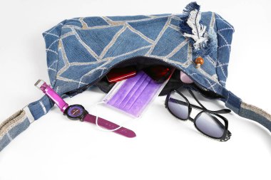 Kot pantolonun içinde ve dışında farklı şahsi eşyalar, gözlük ve saat olan kadın el yapımı çanta. Beyaz yüzeyde yakın plan