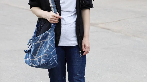 Part of the body of woman in jeans, which keeps bag made of denim tissue on her shoulder