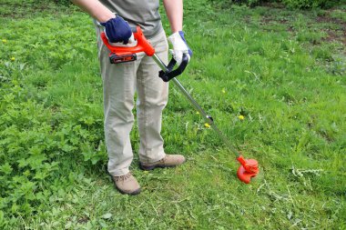 Man holds an electric trimmer in his hands and mow grass in meadow