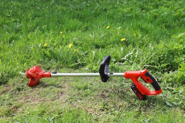 Manual electric trimmer for mowing grass in small volumes in garden and courtyard, on background of green meadow