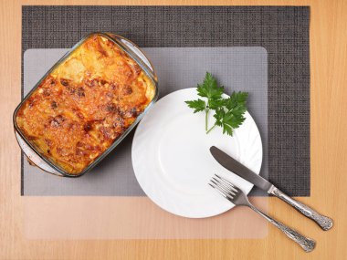 Cam kapta etli patates güveci, temiz beyaz tabak ve düz çatal bıçak.