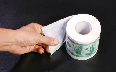 Dolar şeklinde tuvalet kağıdı rulosu, el kenarı açık. Siyah arka planda bütçe açığı ve malların yüksek maliyeti kavramı
