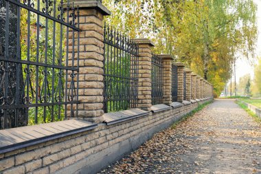Demirden çitlerin yanındaki ıssız yolda demirden yapılmış kafesler, sonbahar tonlarında dökülen yapraklarla doğrusal perspektif.