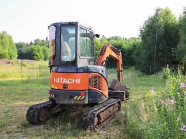 Sergiev Posad, Rusya - 28 Haziran 2021: Küçük Hitachi Kazıcısı yaz aylarında kırsal alanda inşaat için boş yeşil bir alanda, dikiz manzaralı