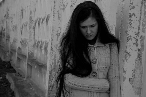 Плачущая девушка в депрессии стоит, прислонившись к старой стене.