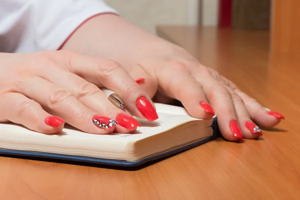 Female hands with manicure over pages of a notebook — Stock Photo, Image
