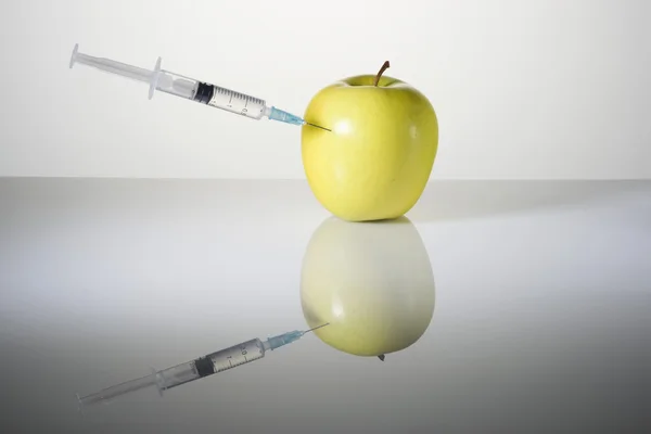 A seringa com a agulha empurrada em maçã verde — Fotografia de Stock
