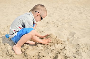 Küçük çocuk kum sahilde oynarken.