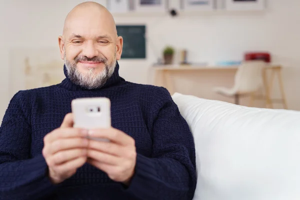 Uomo sorridente che controlla i messaggi del telefono cellulare a casa — Foto Stock