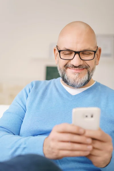 Usmívající se dospělý muž s mobilním telefonem v domácnosti — Stock fotografie