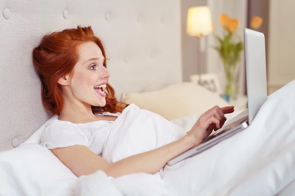 Feliz joven pelirroja mujer usando el ordenador portátil en la cama —  Fotos de Stock