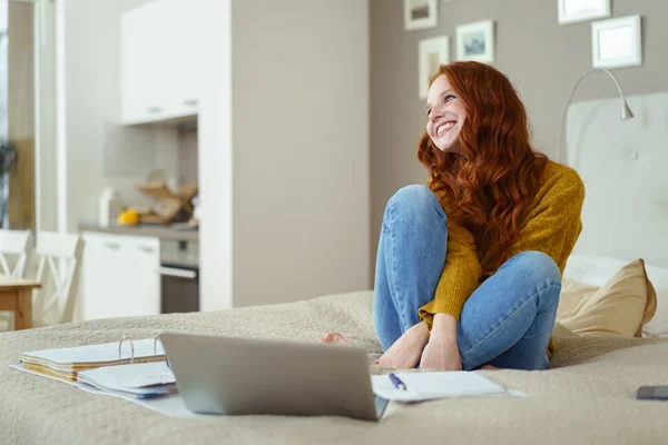 Glückliche junge Frau mit Laptop und Papieren im Bett — Stockfoto