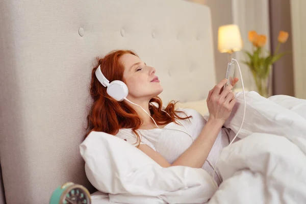 Mladá zrzka žena relaxační hudbou v posteli — Stock fotografie