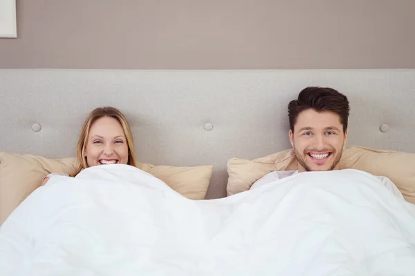 Игривая молодая пара лежит в постели ухмыляясь — стоковое фото
