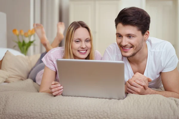 Casal jovem deitado em uma cama com um laptop — Fotografia de Stock