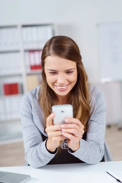 Glückliche Frau schaut im Büro auf Handy — Stockfoto