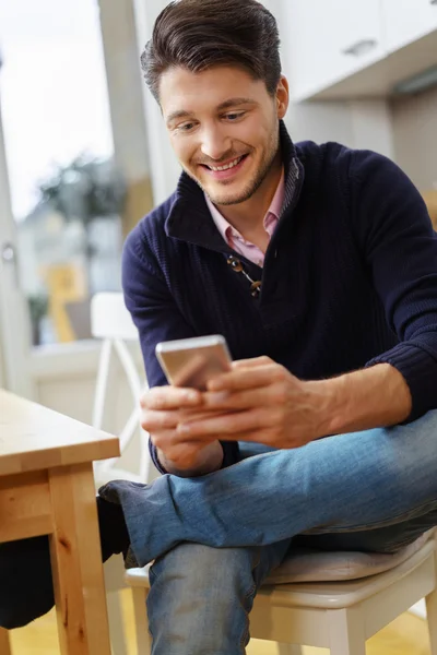 Young man sitting in the kitchen with his mobile — Stock Photo, Image