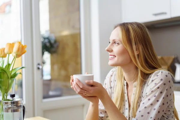 Grinning blond woman with cup in kitchen — Stock Photo, Image