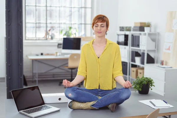 Woman sitting on desk in meditative pose — Stock fotografie