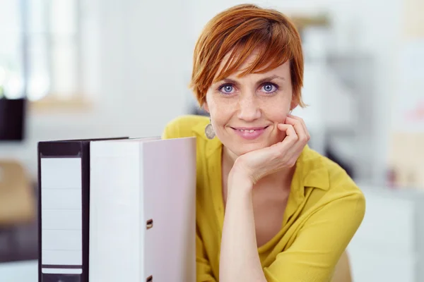 Mujer sonriente junto a carpetas en el trabajo — Foto de Stock