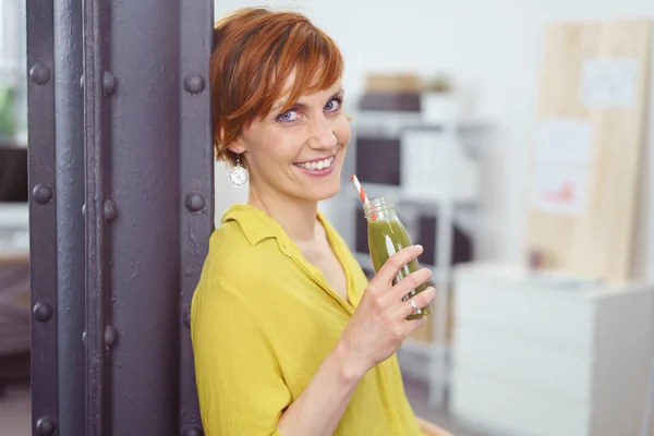 Mignon jeune femme aux cheveux rouges sirotant du jus vert — Photo