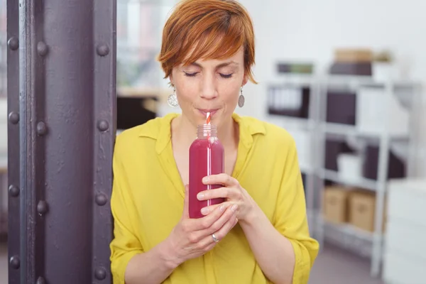 Thirsty woman sipping fruit juice at office — Stock Photo, Image