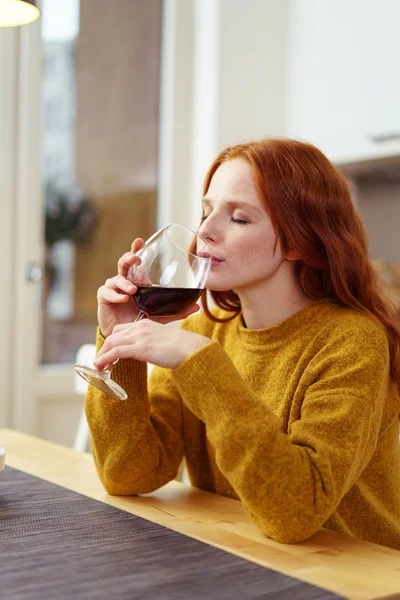 Schöne Frau nippt Wein am Küchentisch — Stockfoto