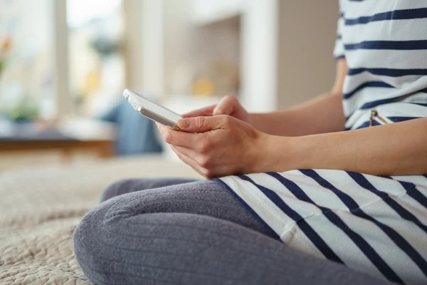 Woman kneeling on her bed with her mobile — Stockfoto