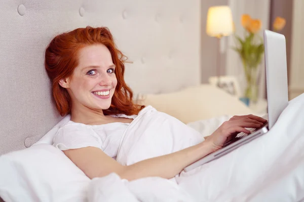 Mujer joven relajándose en la cama con su portátil — Foto de Stock