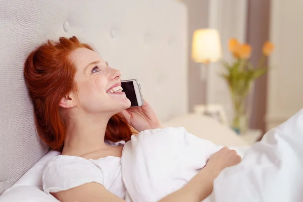 Mujer joven sonriendo mientras charla en un móvil — Foto de Stock