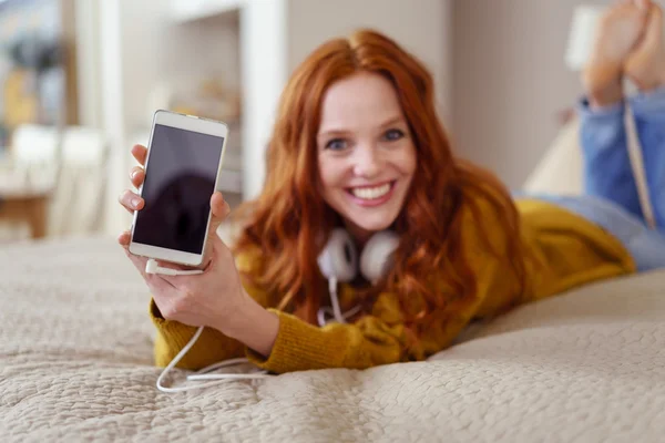 Mujer joven feliz en la cama mostrando el teléfono móvil — Foto de Stock