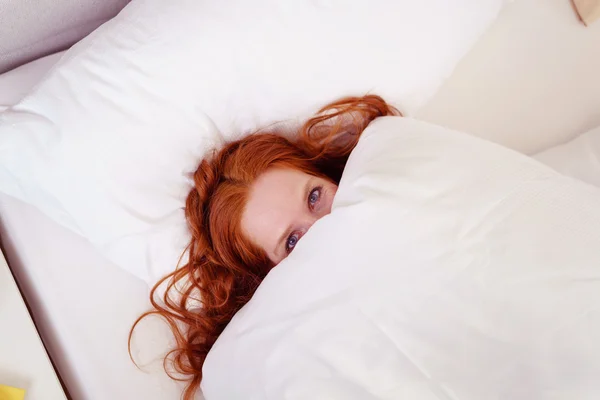 Schüchterne junge Frau versteckt sich unter der Bettdecke — Stockfoto