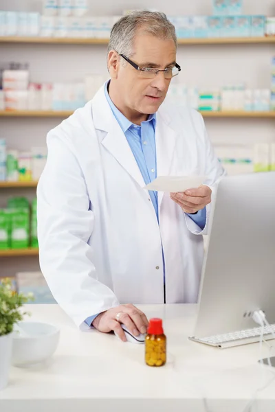 Serious pharmacist in lab coat with prescription — Stock Photo, Image