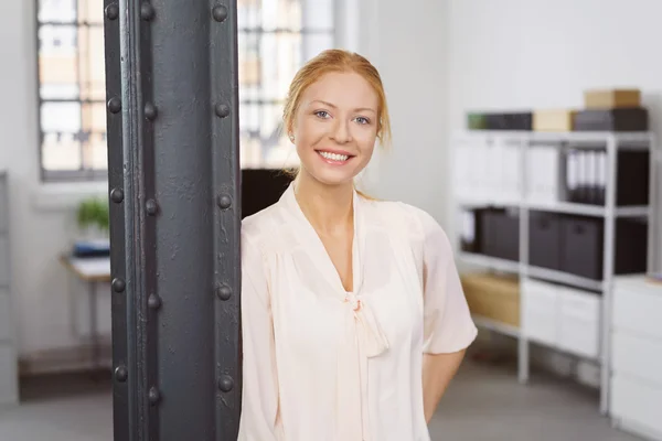 Attractive smiling woman leaning on post at work — Stock Photo, Image