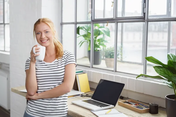 Lächelnde Frau steht neben Fenster am Schreibtisch — Stockfoto
