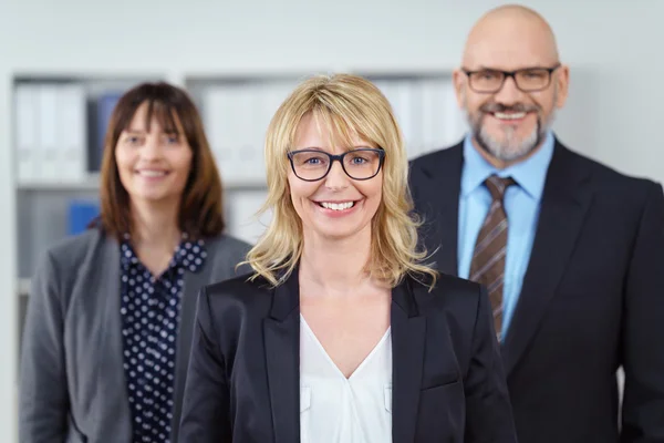 Three business people smile at camera near shelf — Stock Photo, Image
