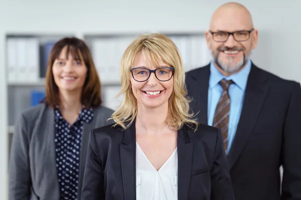 Tre affärsmänniskor leende på kameran nära hyllan — Stockfoto