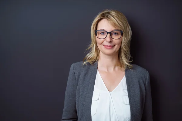 Grinning woman in eyeglasses in front of wall — Stock Photo, Image