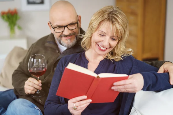 Man peeking over his wife's shoulder as she reads — Stock Photo, Image