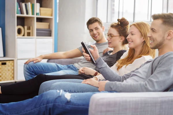 Quattro amici si rilassano e guardano la televisione in camera — Foto Stock