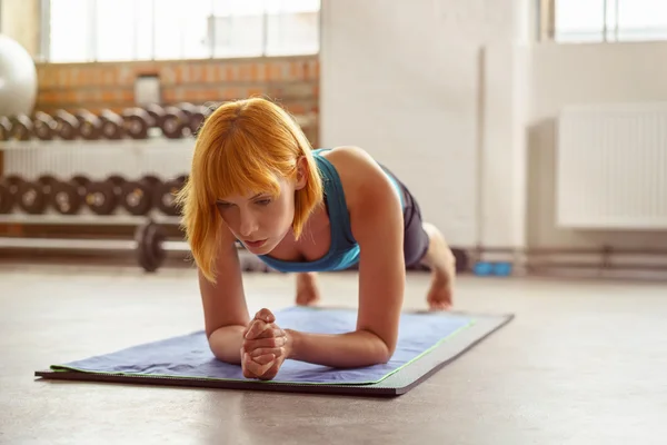 Mujer joven en la posición de planchado en una alfombra de gimnasio —  Fotos de Stock