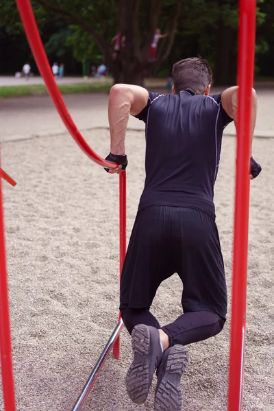 Young man working out on curved bars in a park — Stock Photo, Image