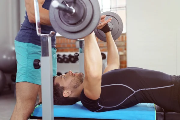 Spotter helping man perform bench presses — Stock Photo, Image