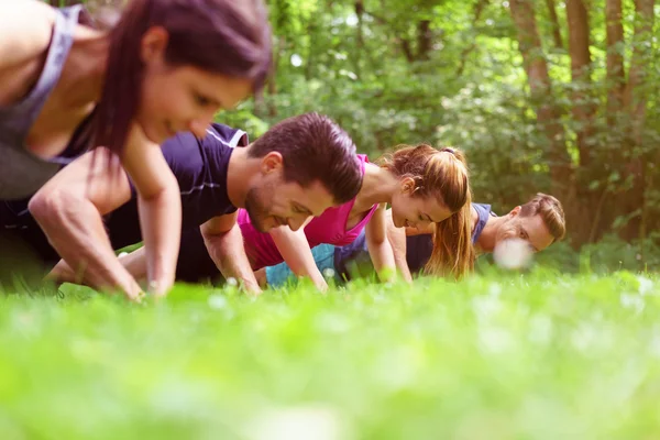 Vier jongeren doen push-ups in een park — Stockfoto