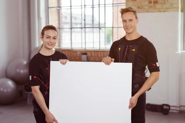 Dos instructores de fitness en un gimnasio sosteniendo un cartel — Foto de Stock