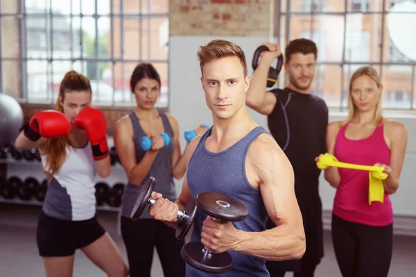 Hombre musculoso sosteniendo mancuernas con grupo en la parte trasera — Foto de Stock