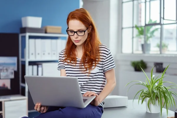 Young businesswoman sitting perched on her desk — ストック写真