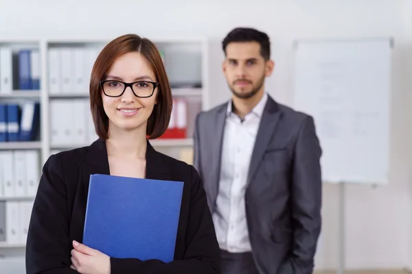 Woman holding blue folder with man in background — 스톡 사진