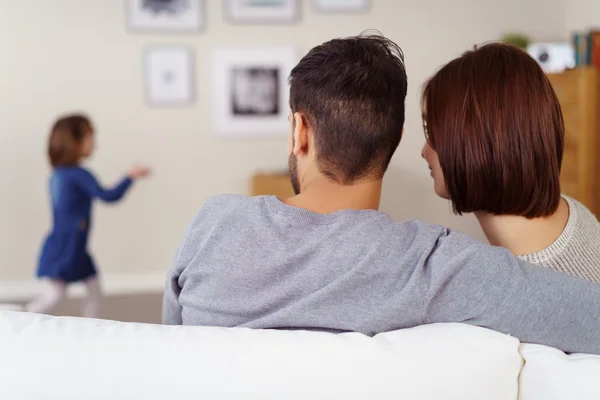 Jovem casal sentado assistindo sua filha jogar — Fotografia de Stock